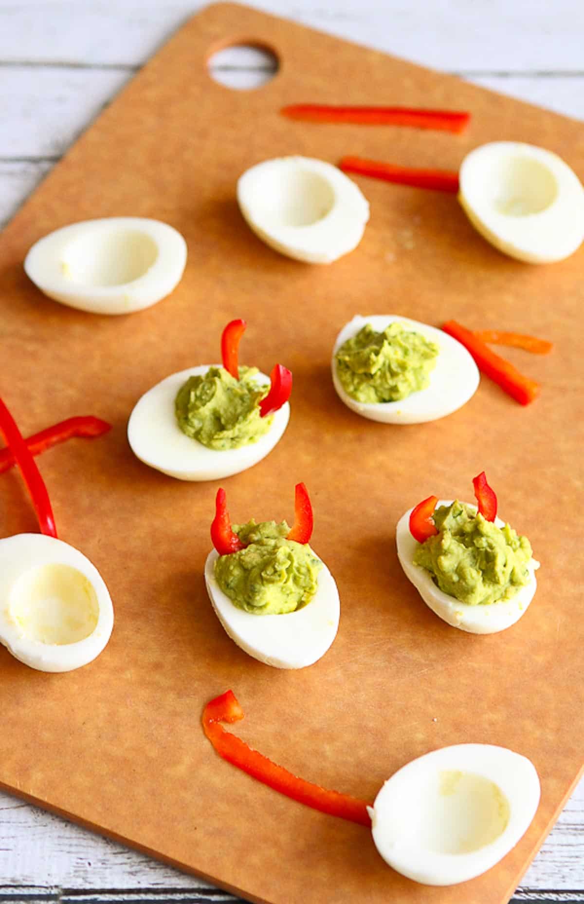 Deviled eggs with red pepper pieces, all on a cutting board.