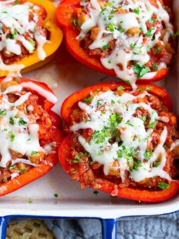 Cheese-topped vegetarian stuffed peppers in a blue baking dish.