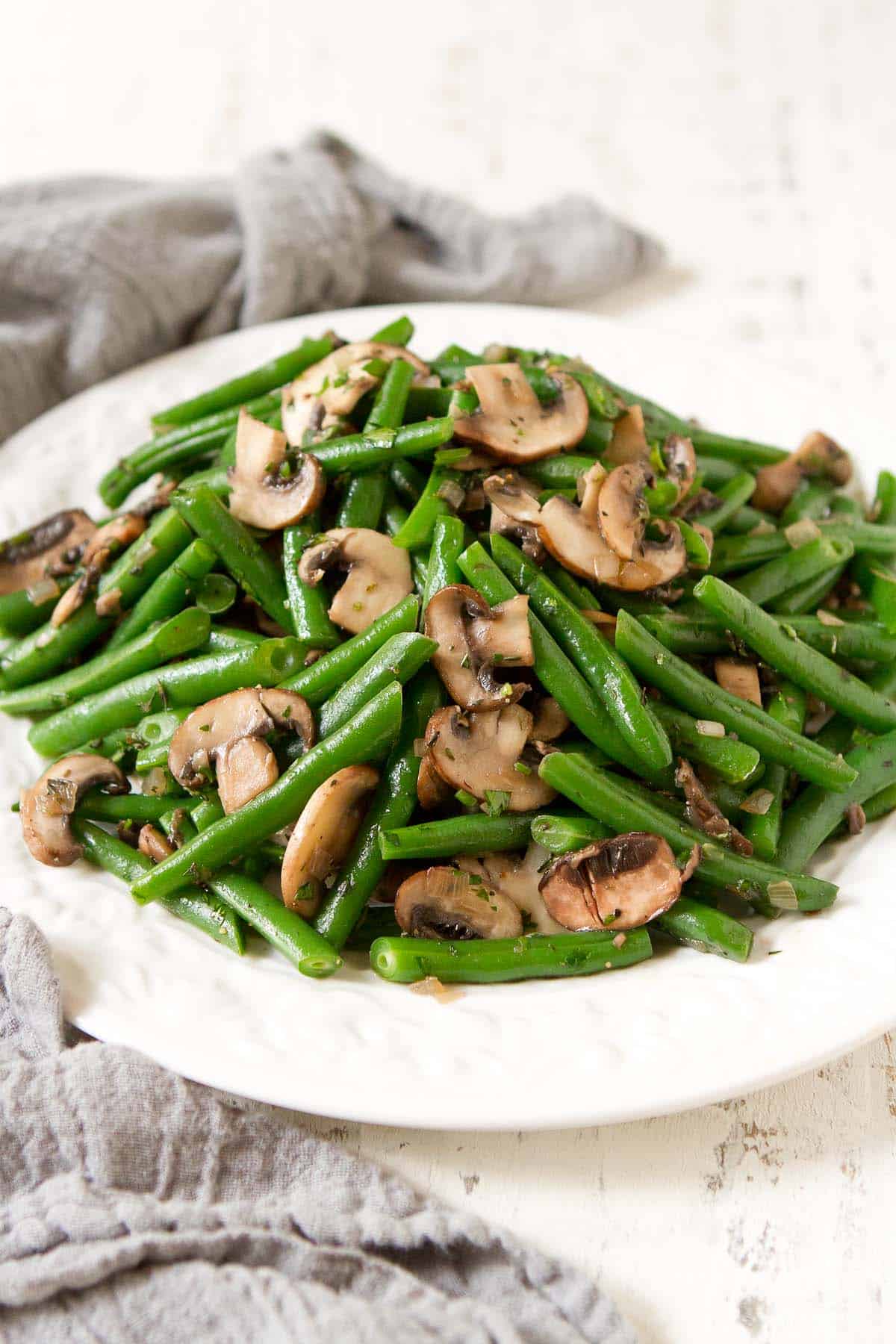 Green bean and mushroom side dish on a white plate, with gray napkin.