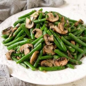 Sautéed green beans and mushrooms on a white plate, with a gray napkin.