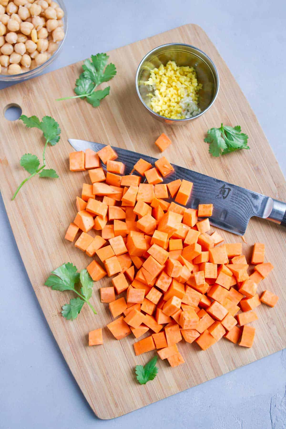 Chopped sweet potato, grated ginger and garlic and chickpeas on a bamboo cutting board.