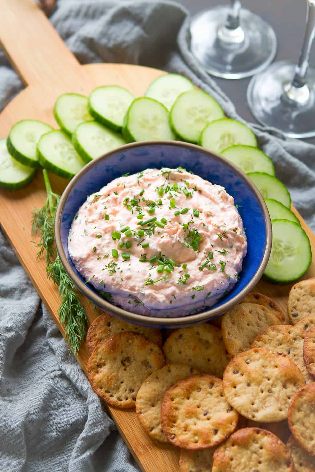 Smoked salmon spread in a bowl on a serving board with cucumber slices and crackers.