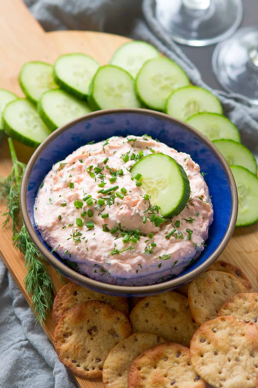 Smoked salmon dip in a blue bowl, surrounded by cucumber slices and crackers.