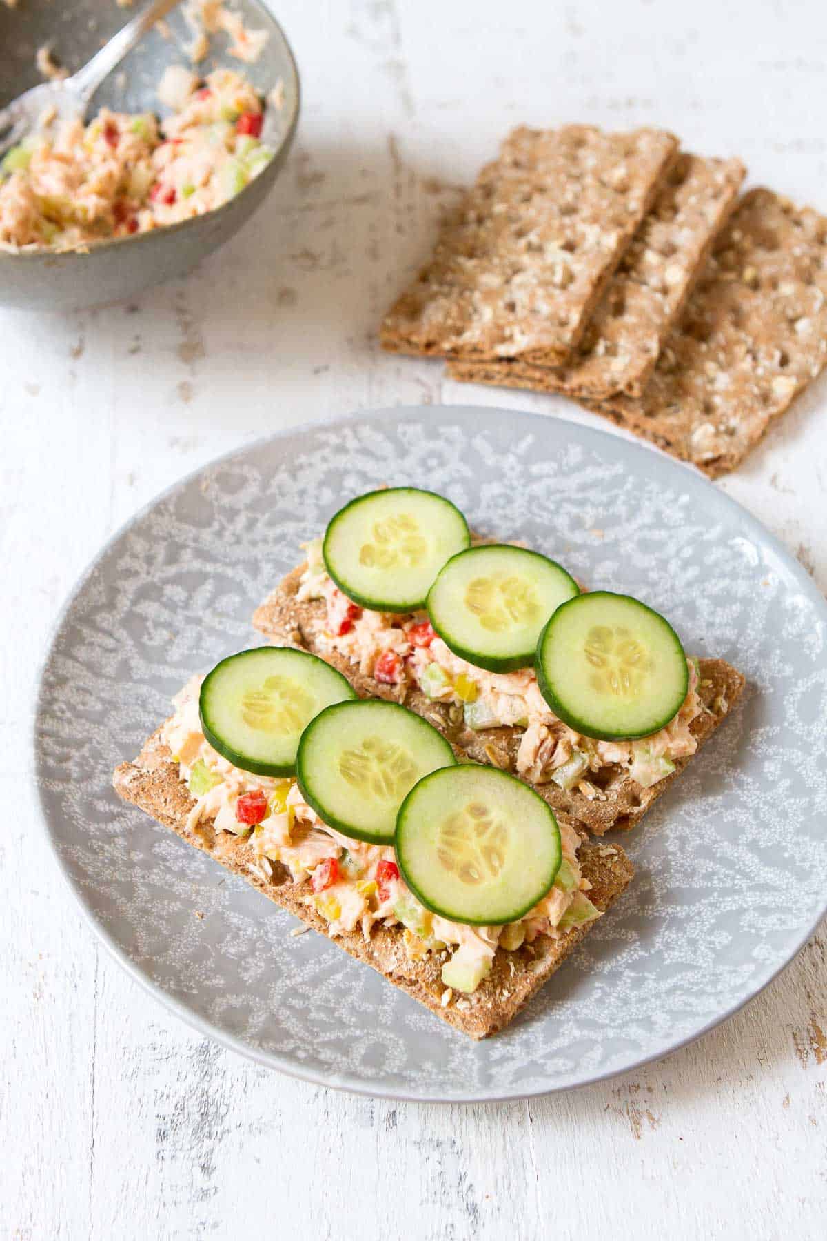 Tuna salad on crackers with cucumber on a gray plate.