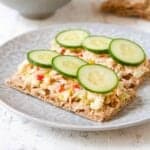 Tuna salad and cucumbers on crackers, on a gray plate.