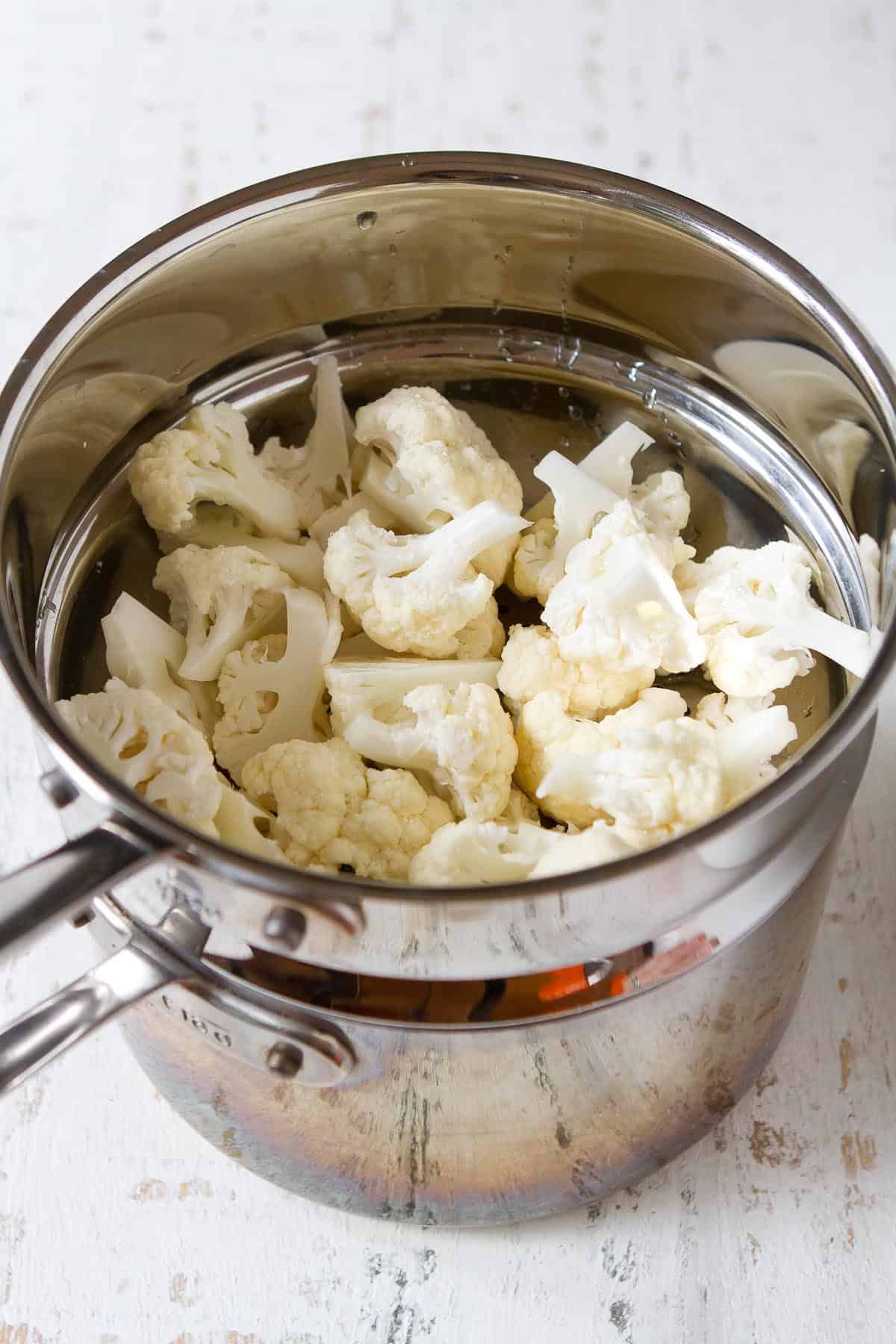 Raw cauliflower florets in a steamer insert.