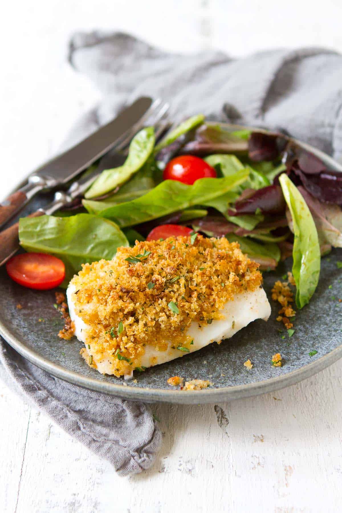 Baked breaded cod with a side salad on a gray plate.