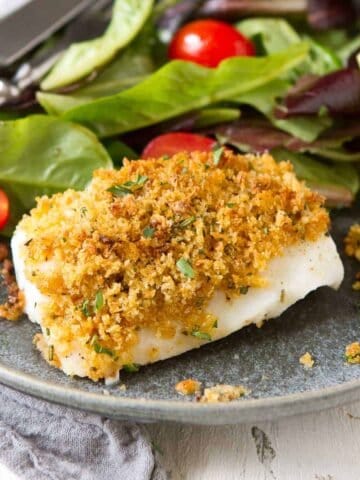 Fish fillet topped with breadcrumbs on a plate, with side salad.