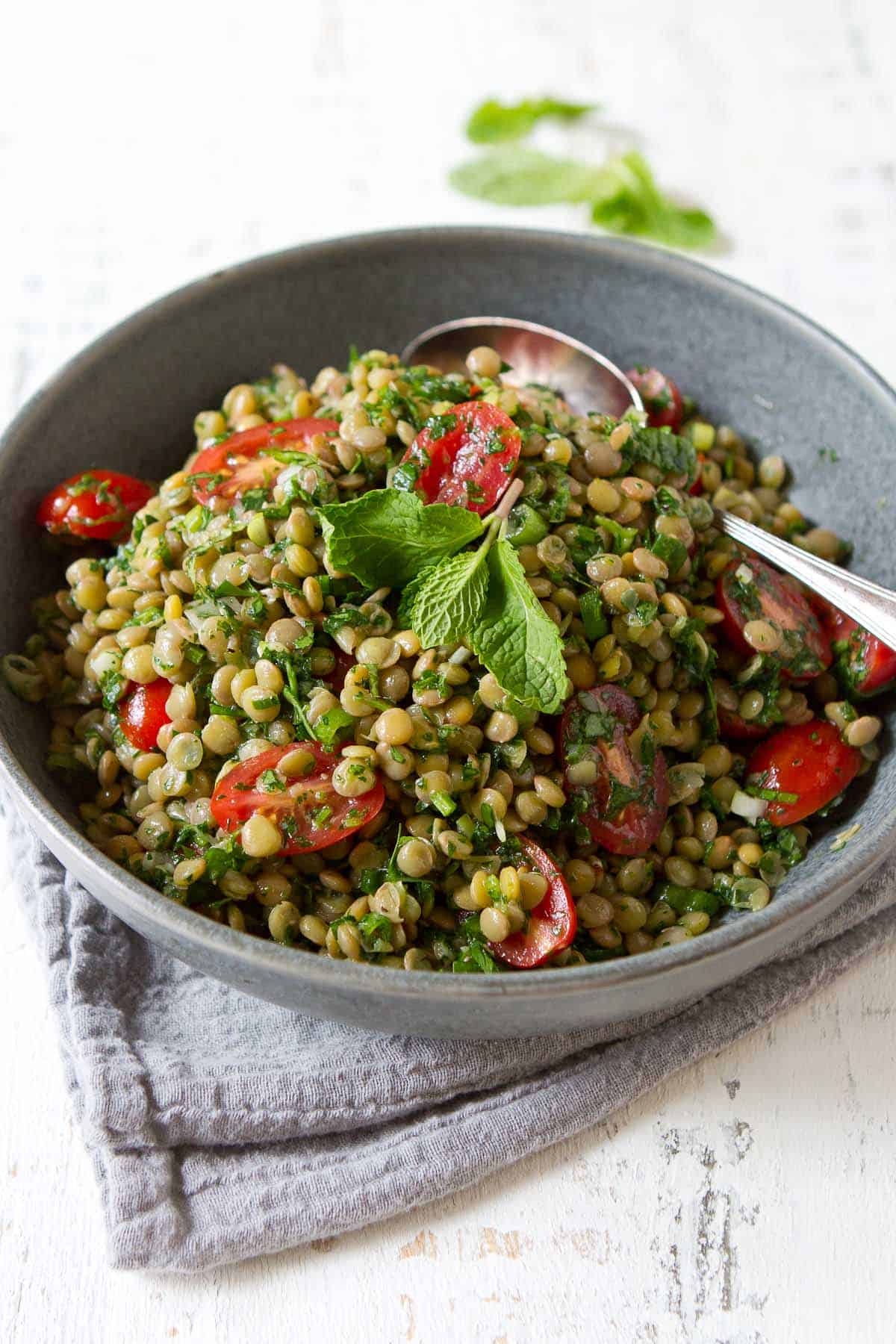 Lentil salad with tomatoes and herbs in a gray bowl.