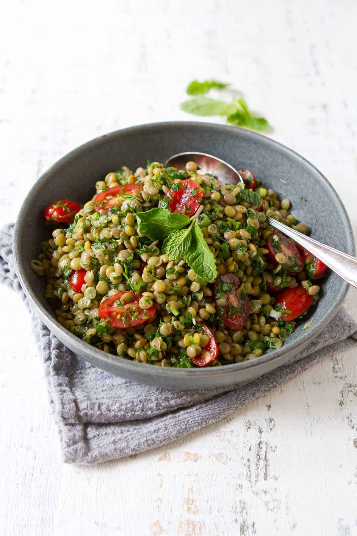 A gray bowl filled with a lentil salad with tomatoes.