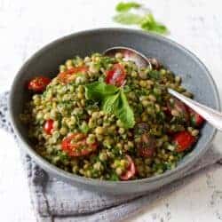 Lentil salad with tomatoes and herbs in a gray bowl.