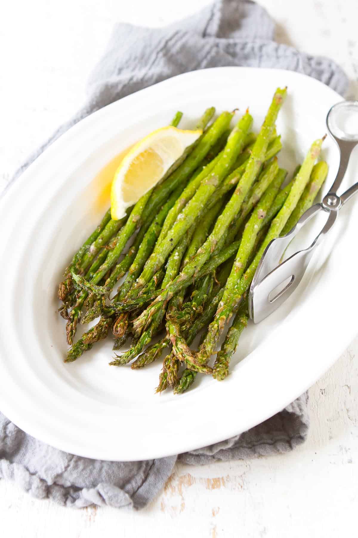Air fryer asparagus and a lemon wedge on a white plate.
