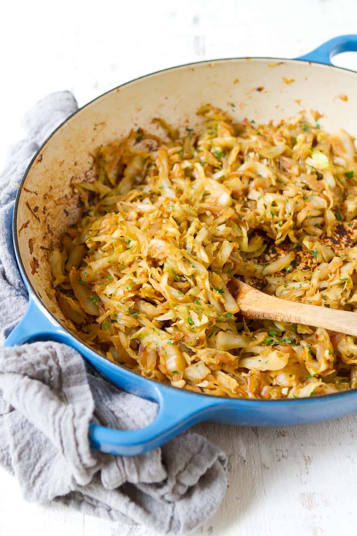 Sauteed cabbage and onions in a large skillet, with a wooden spoon.