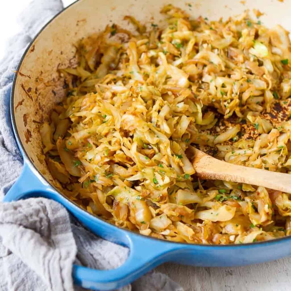 Sauteed green cabbage and a wooden spoon in a large blue skillet.
