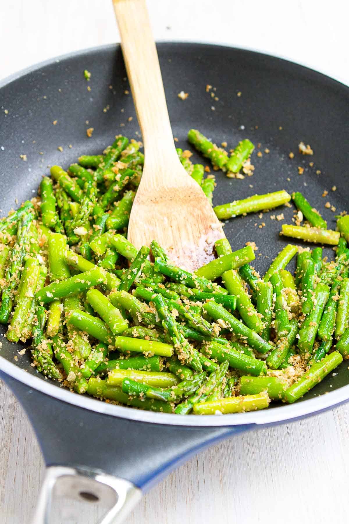 Sauteed asparagus, mixed with garlicky breadcrumbs, in a black skillet.