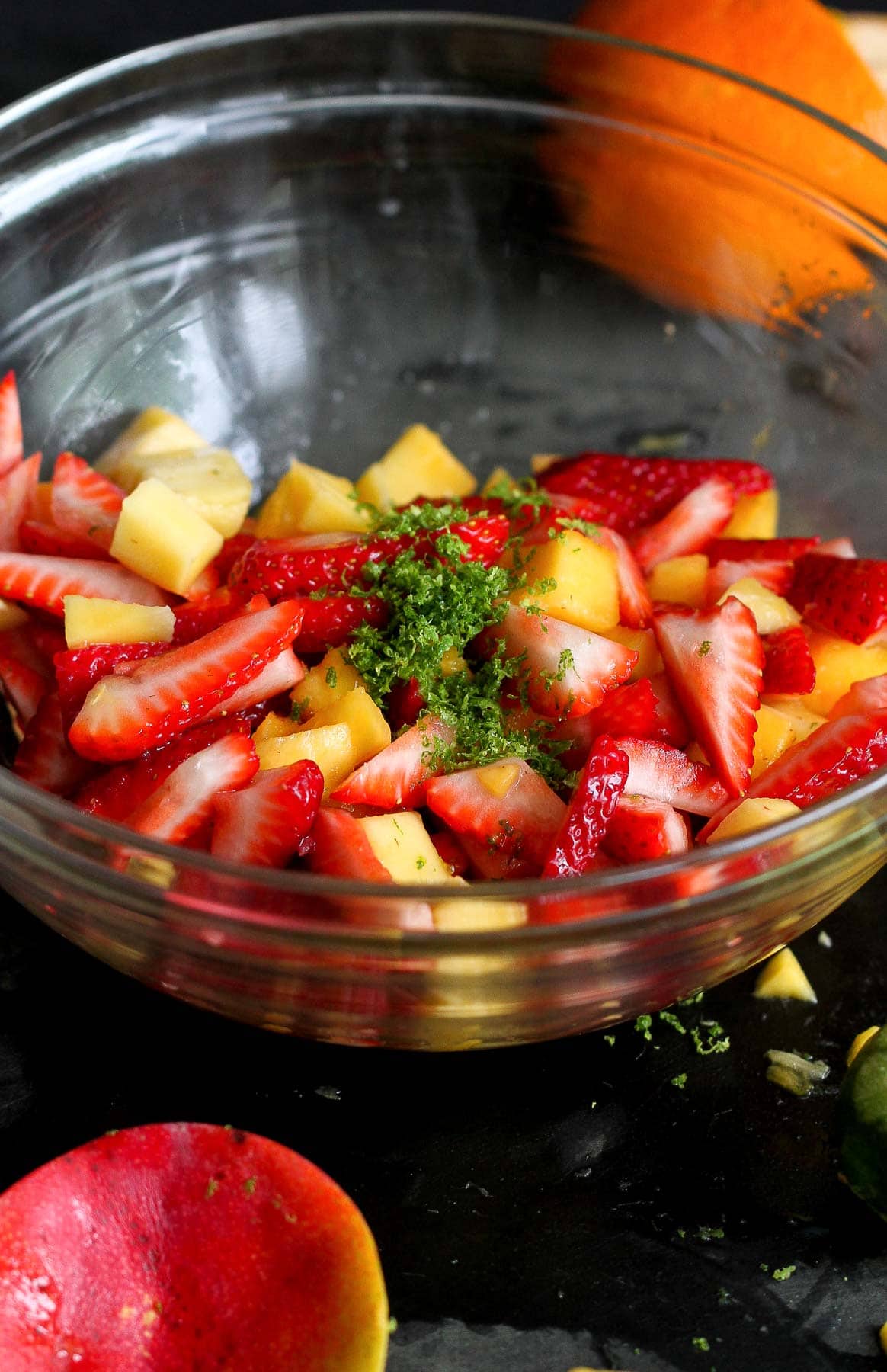 Cut strawberries and mango with lime zest in a large glass bowl.