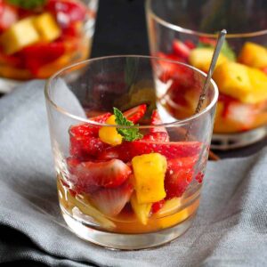 Strawberry mango fruit salad in a short glass with a silver spoon.
