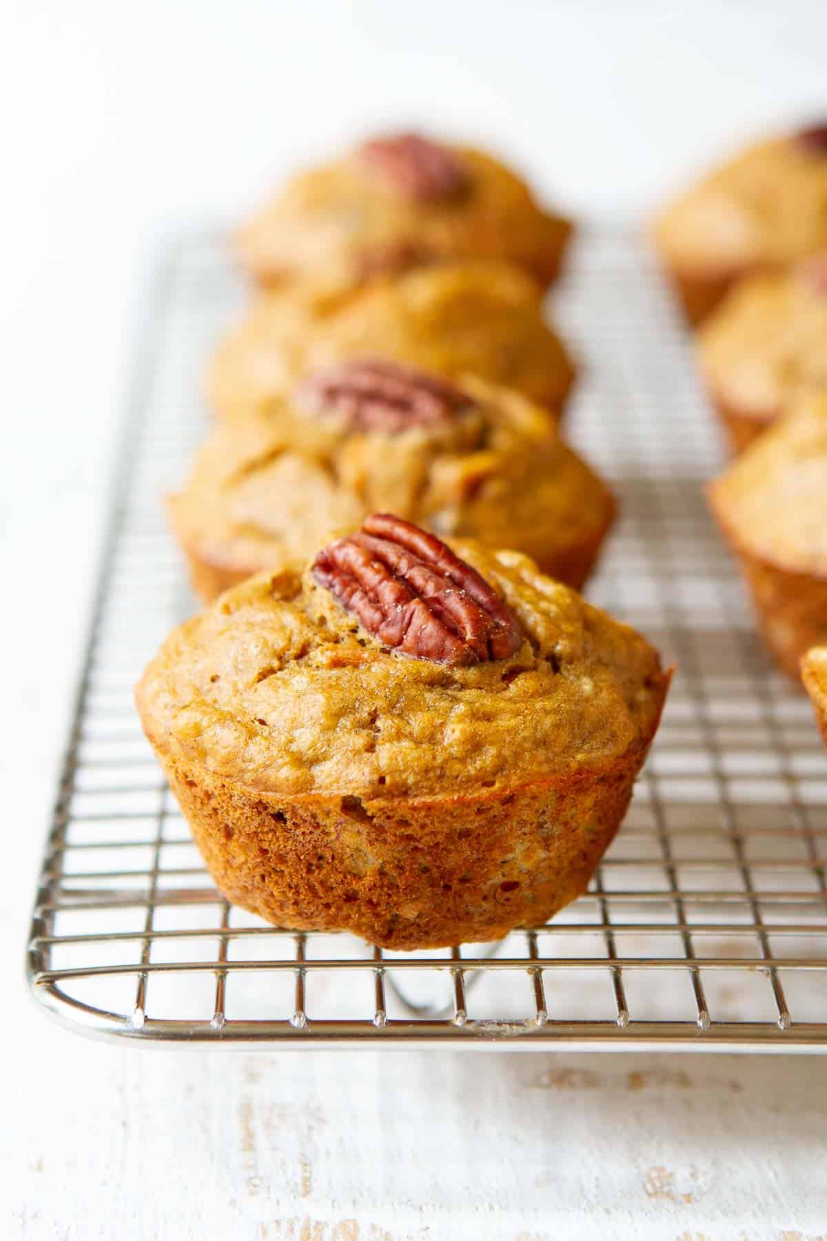 Banana carrot muffins topped with pecans on a wire rack.