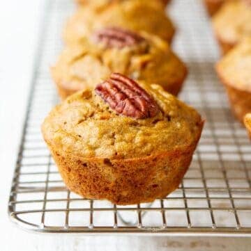 Banana carrot muffins, topped with pecan halves, on a wire rack.