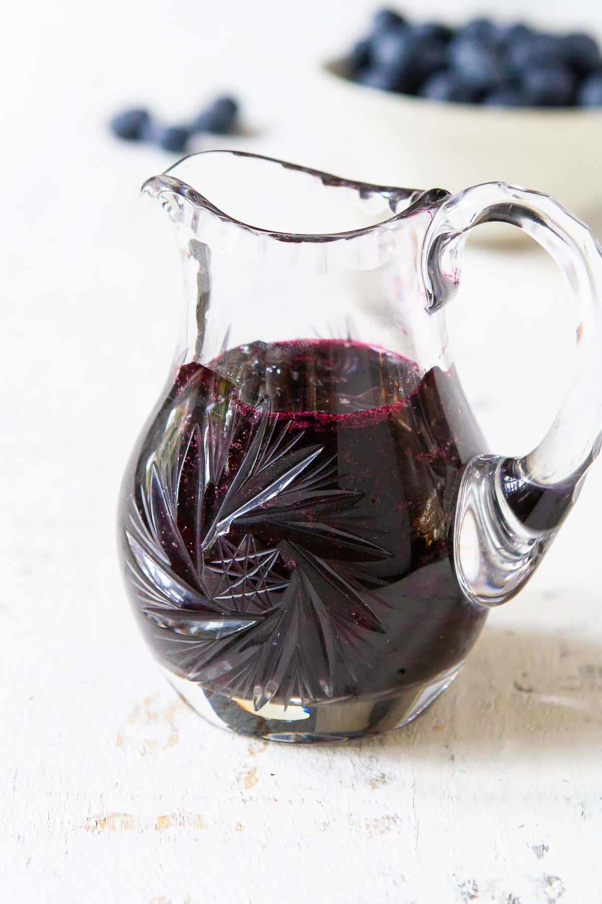 Blueberry syrup in a small crystal pitcher.