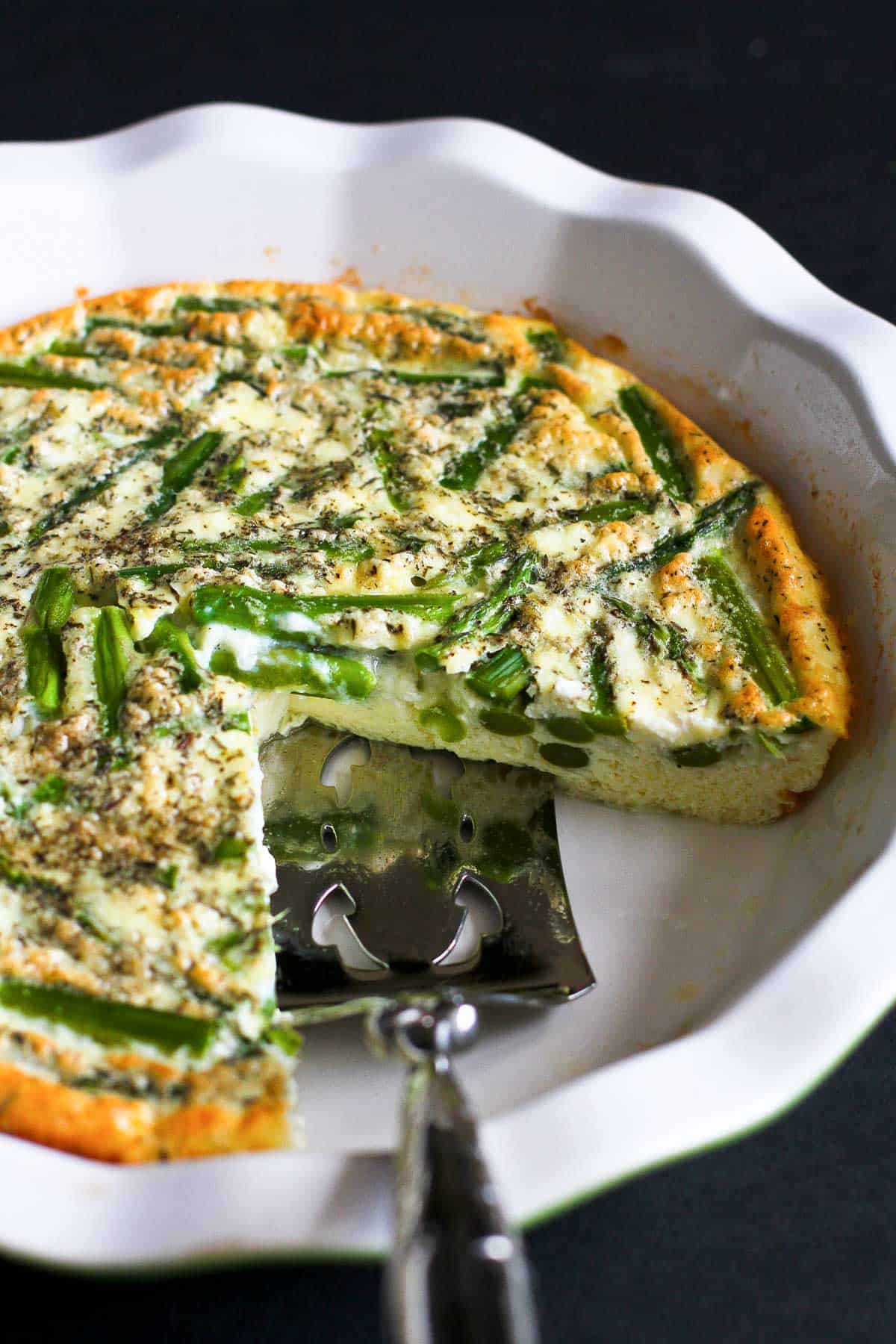 Asparagus quiche in a white pie dish with a silver cake server.