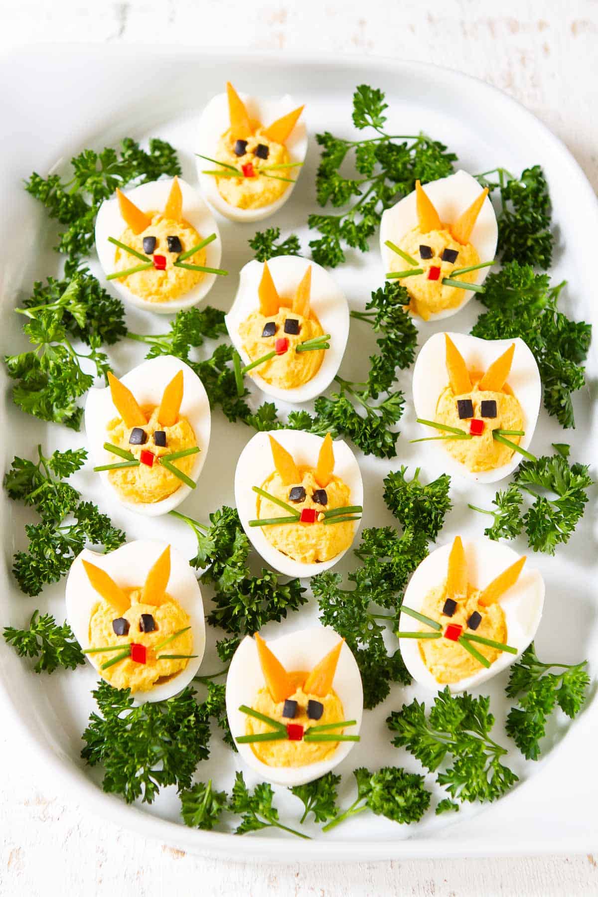 Healthy deviled eggs decorated as bunnies on a white platter.