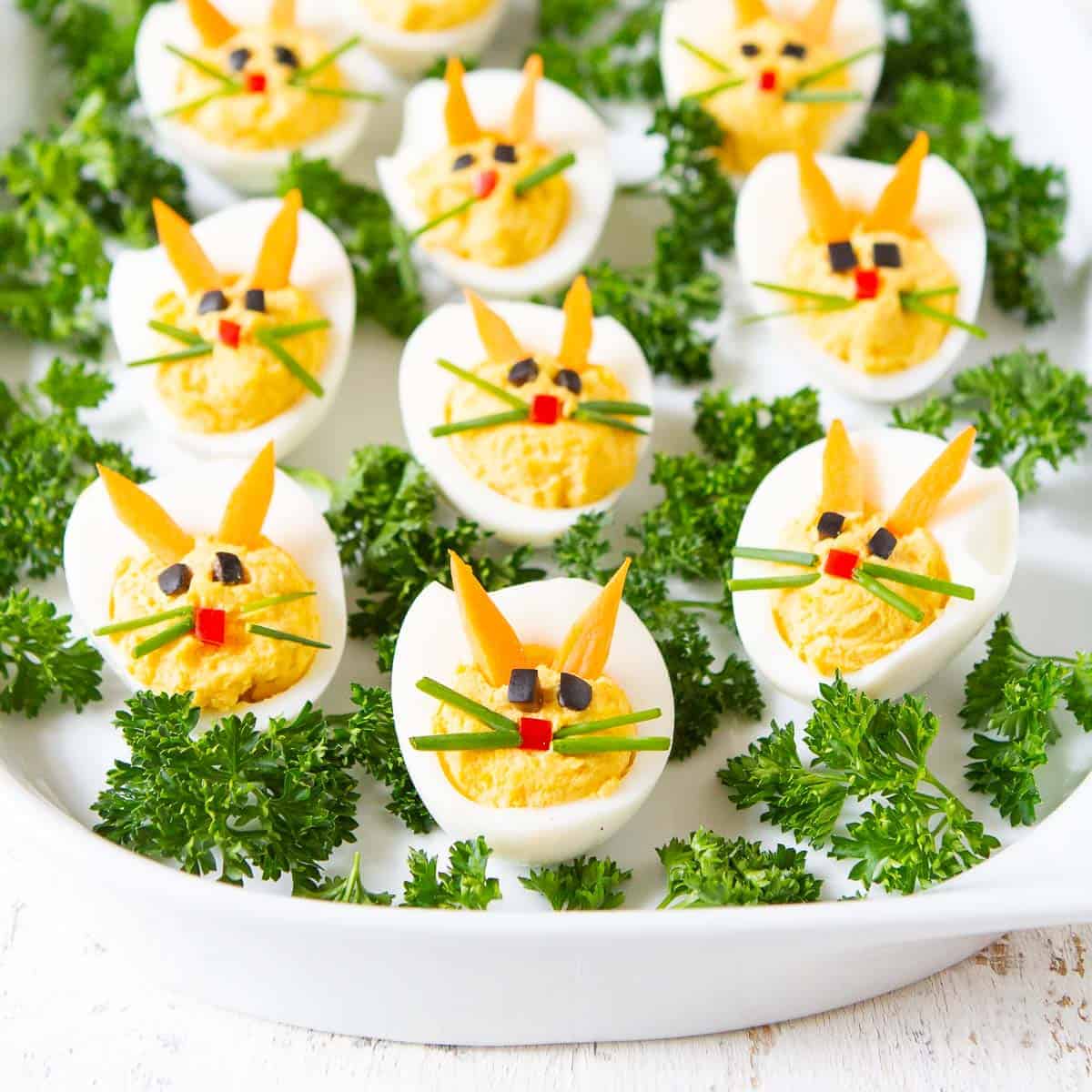 Deviled eggs decorated as bunnies on a white plate.