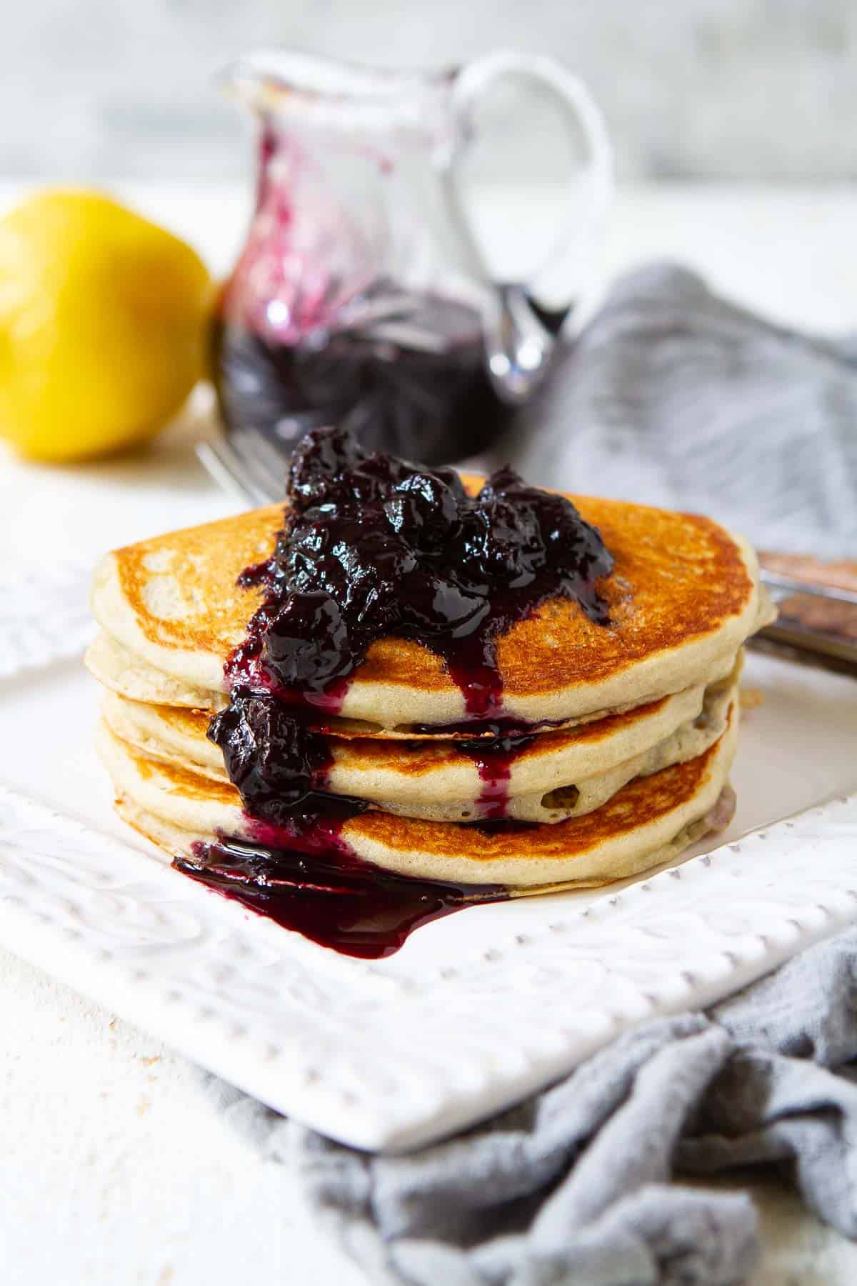 Lemon blueberry pancakes topped with chunky blueberry syrup, on a white plate.