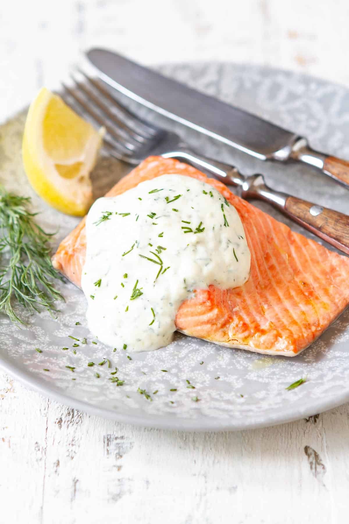 Poached salmon with a yogurt dill sauce on a gray plate.