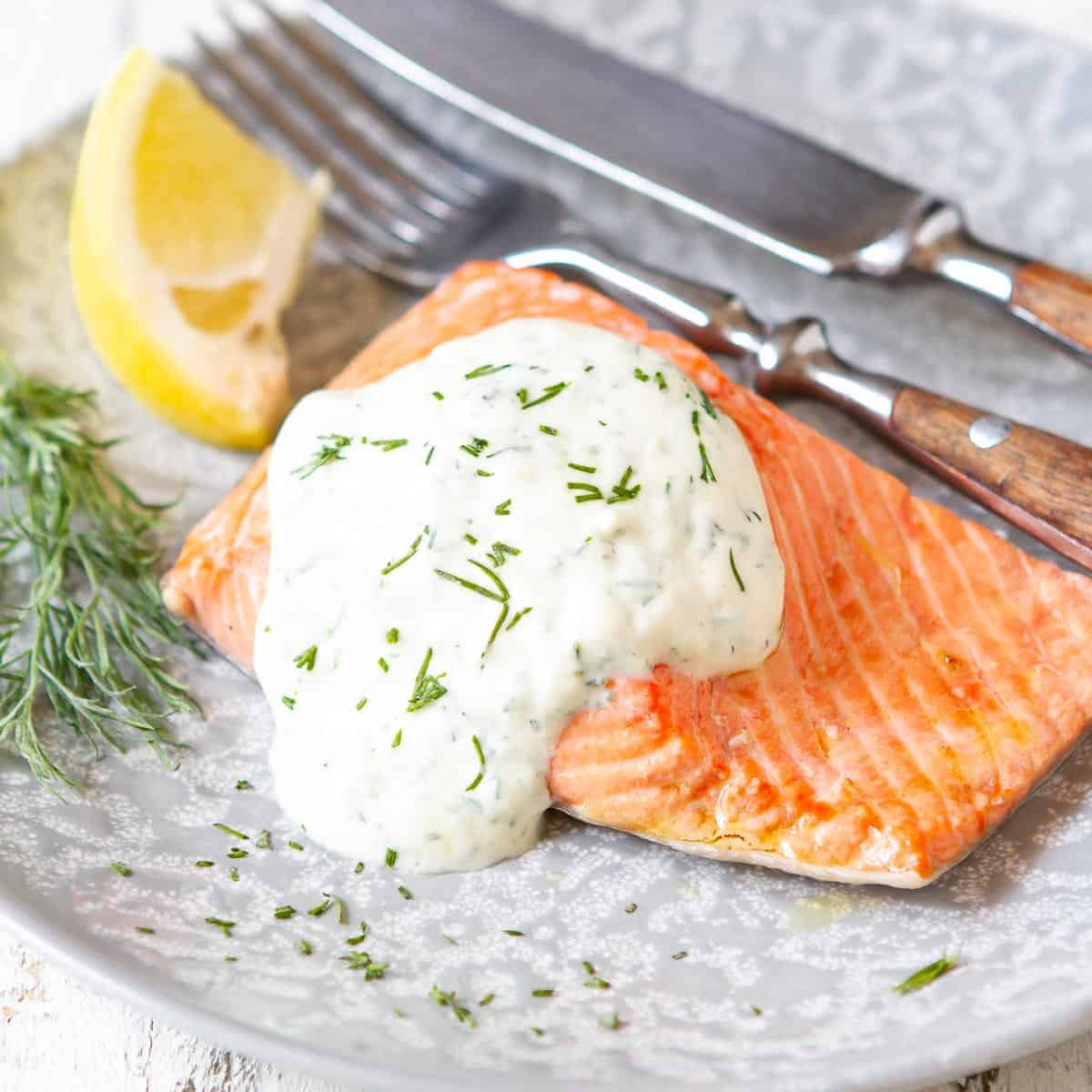 Poached salmon with a yogurt dill sauce on a gray plate.