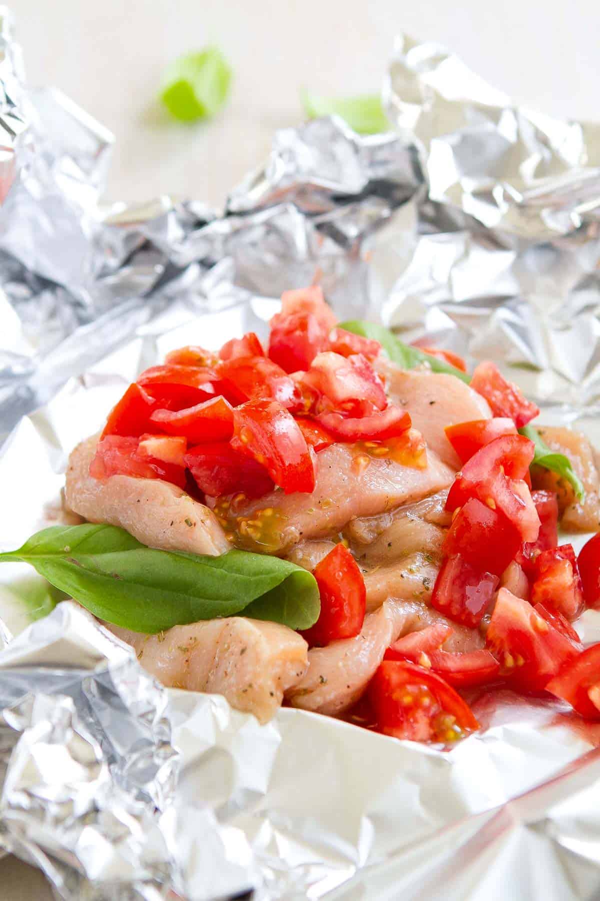 Sliced chicken breast, tomatoes and basil on a sheet of foil.