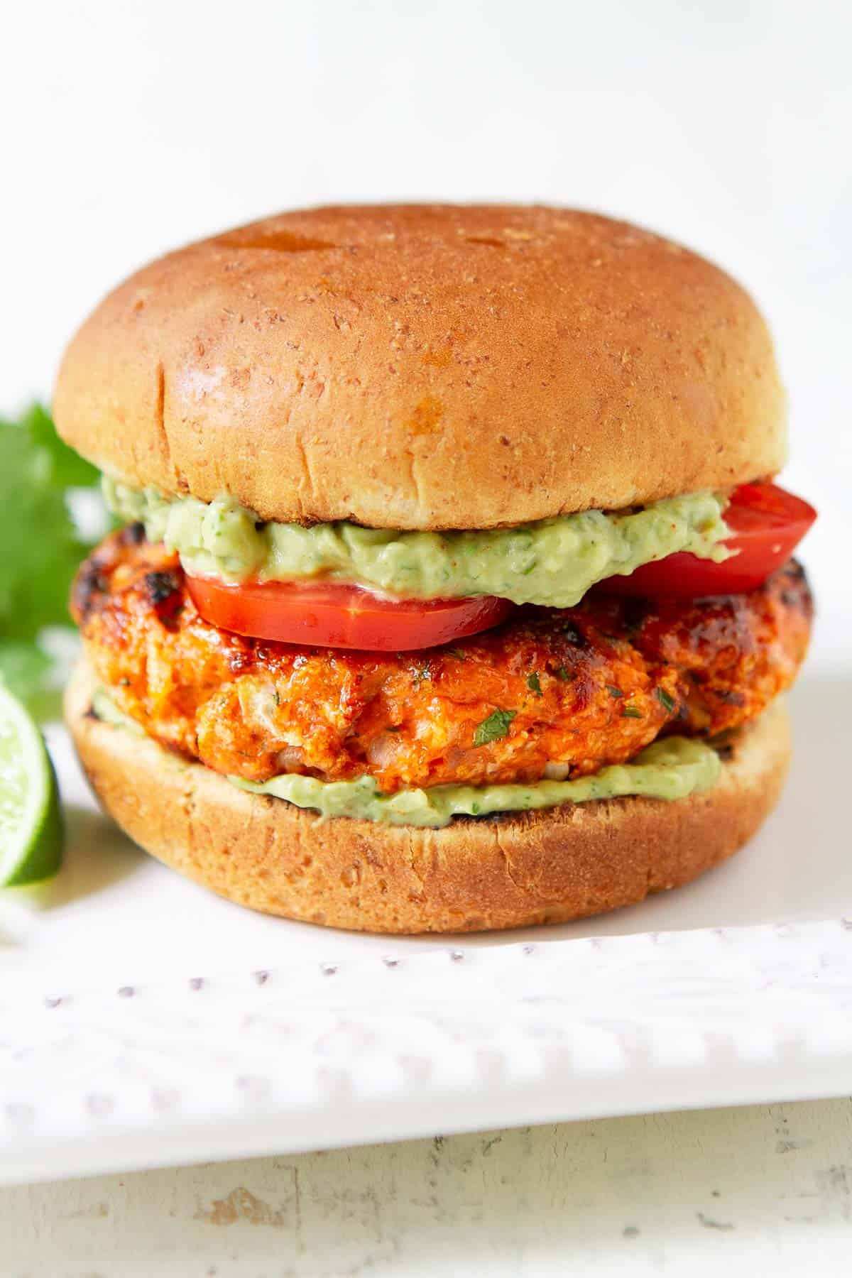 Salmon burger with avocado sauce and tomato on a white plate.