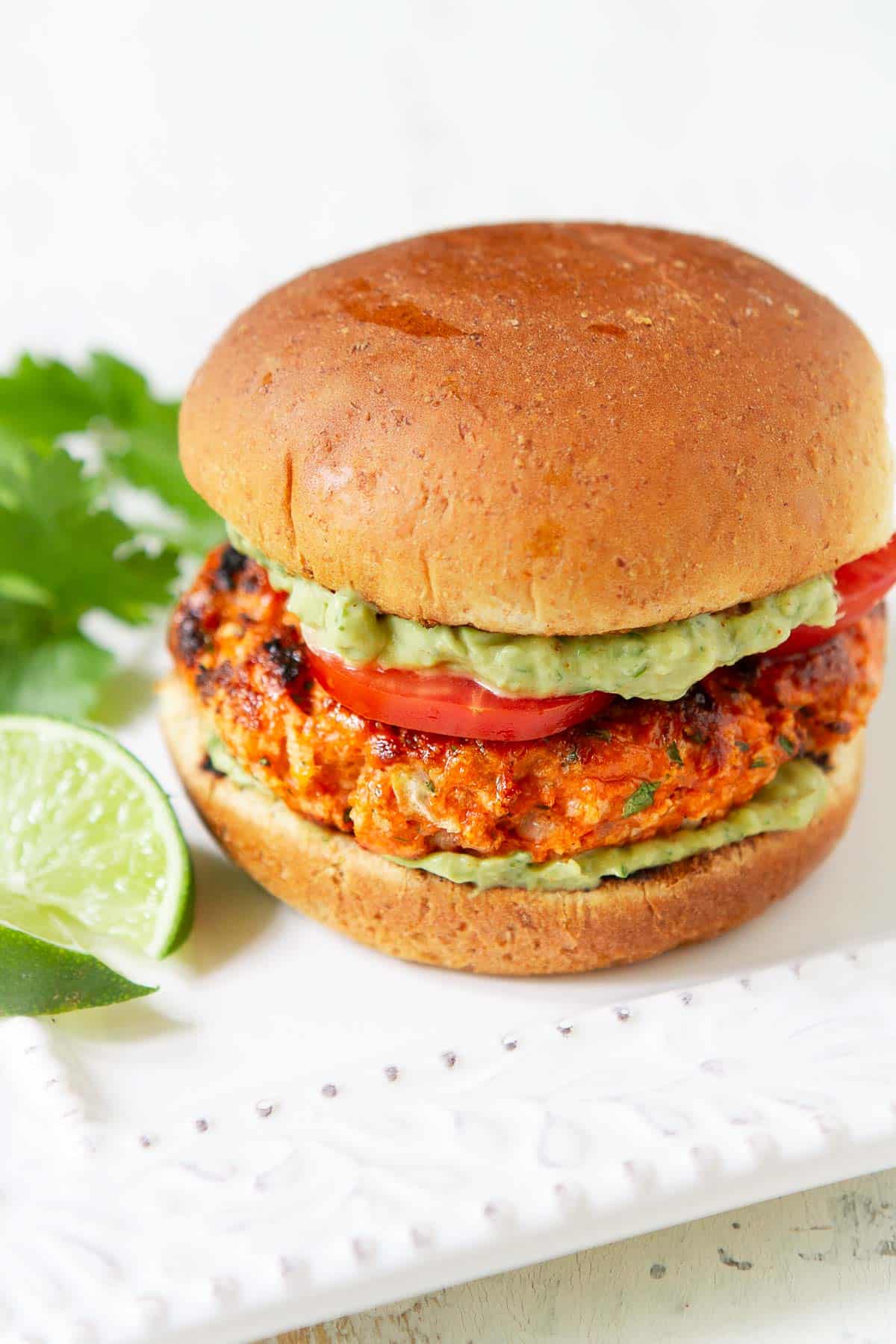 Grilled salmon patty on a bun with avocado sauce and tomato.