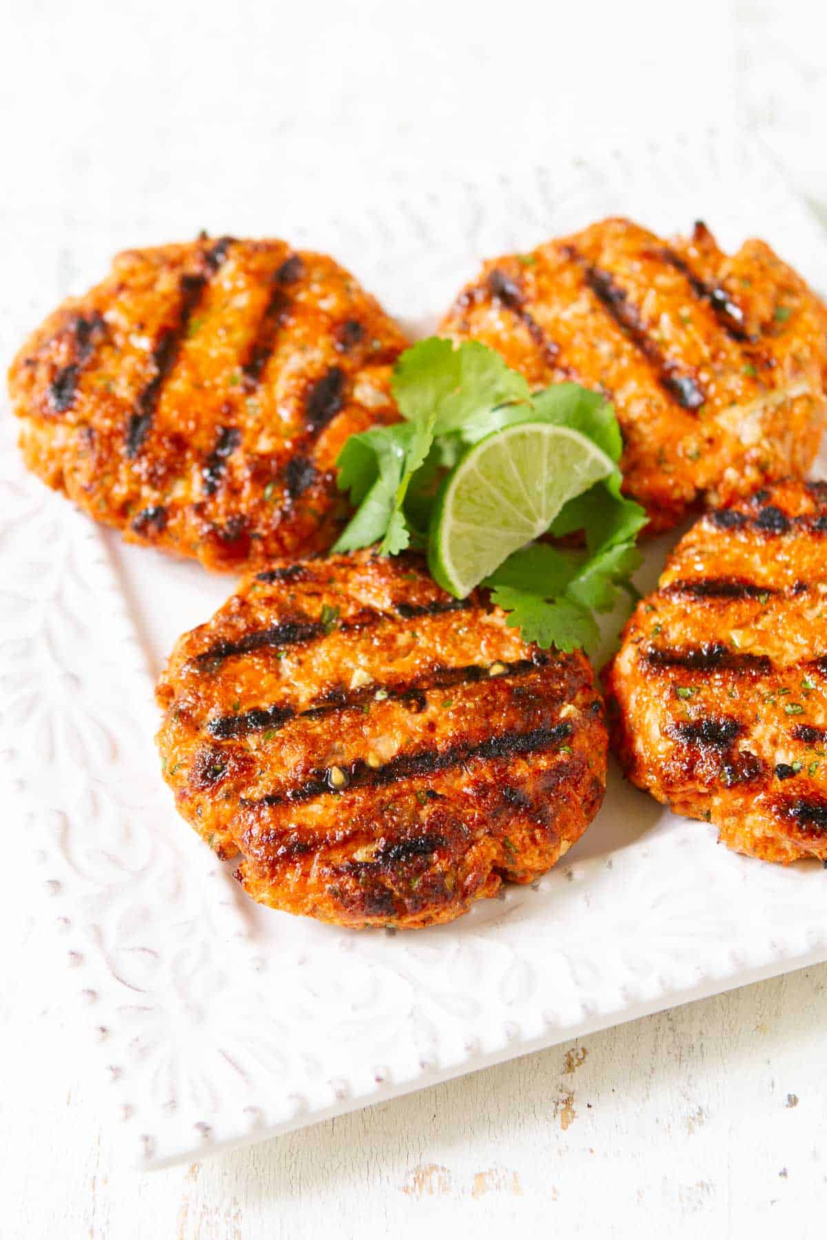 Grilled salmon patties with lime and cilantro on a white plate.