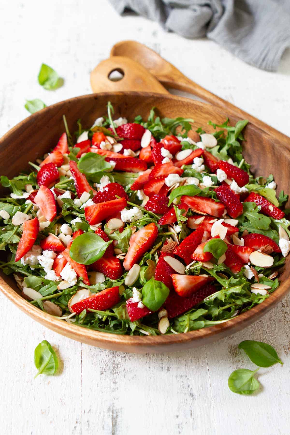 Arugula salad in a wooden salad bowl, with strawberries and cheese.