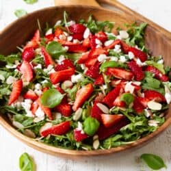 Strawberry arugula salad in with nuts and goat cheese in a wooden salad bowl.