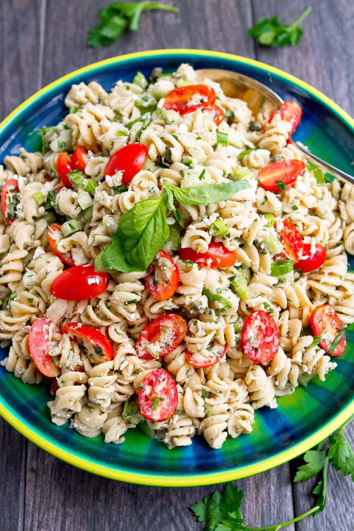 verhead photo of pasta salad with tuna and tomatoes, in a green and blue bowl.