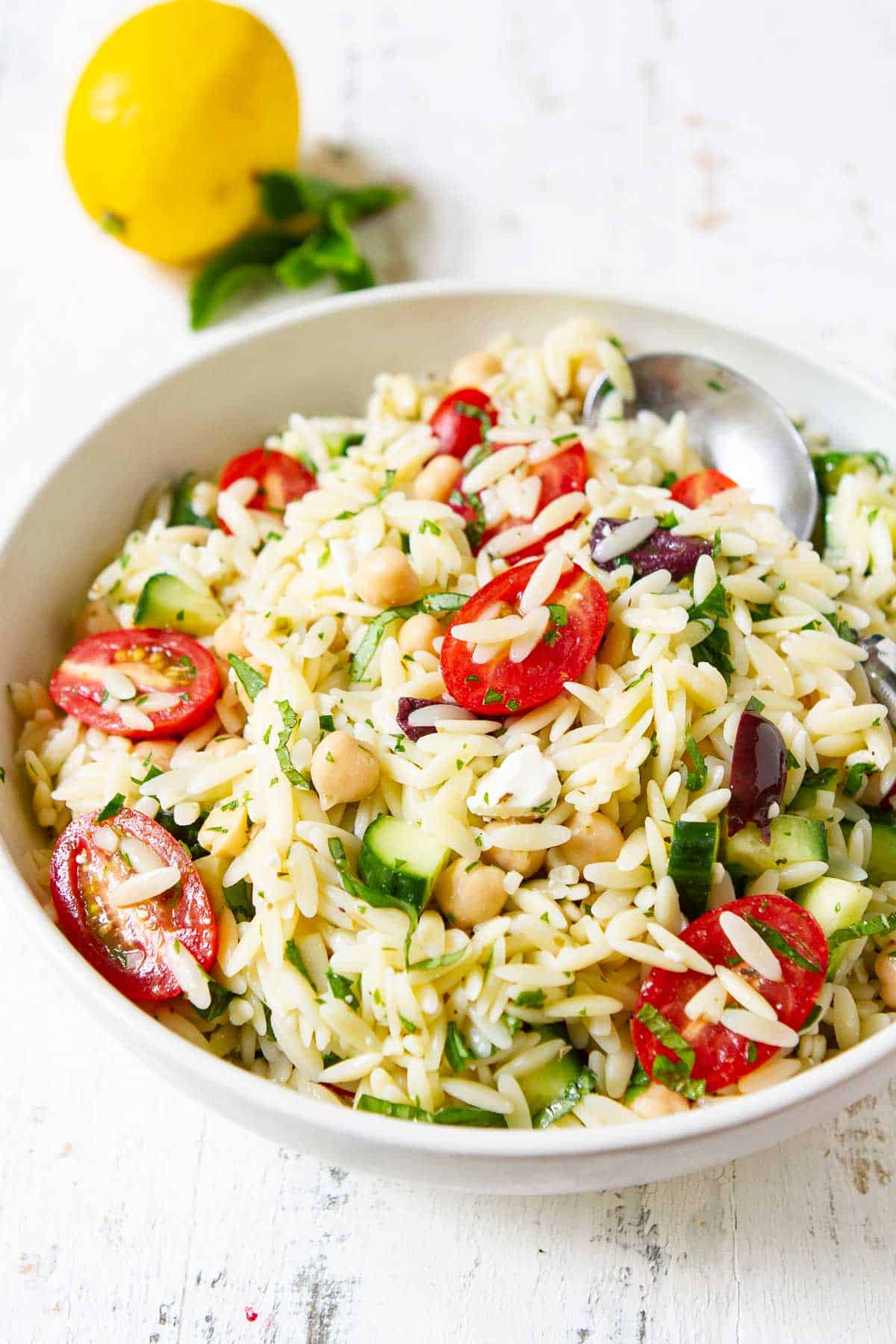 Vegetables, chickpeas and cooked orzo in a white serving bowl.