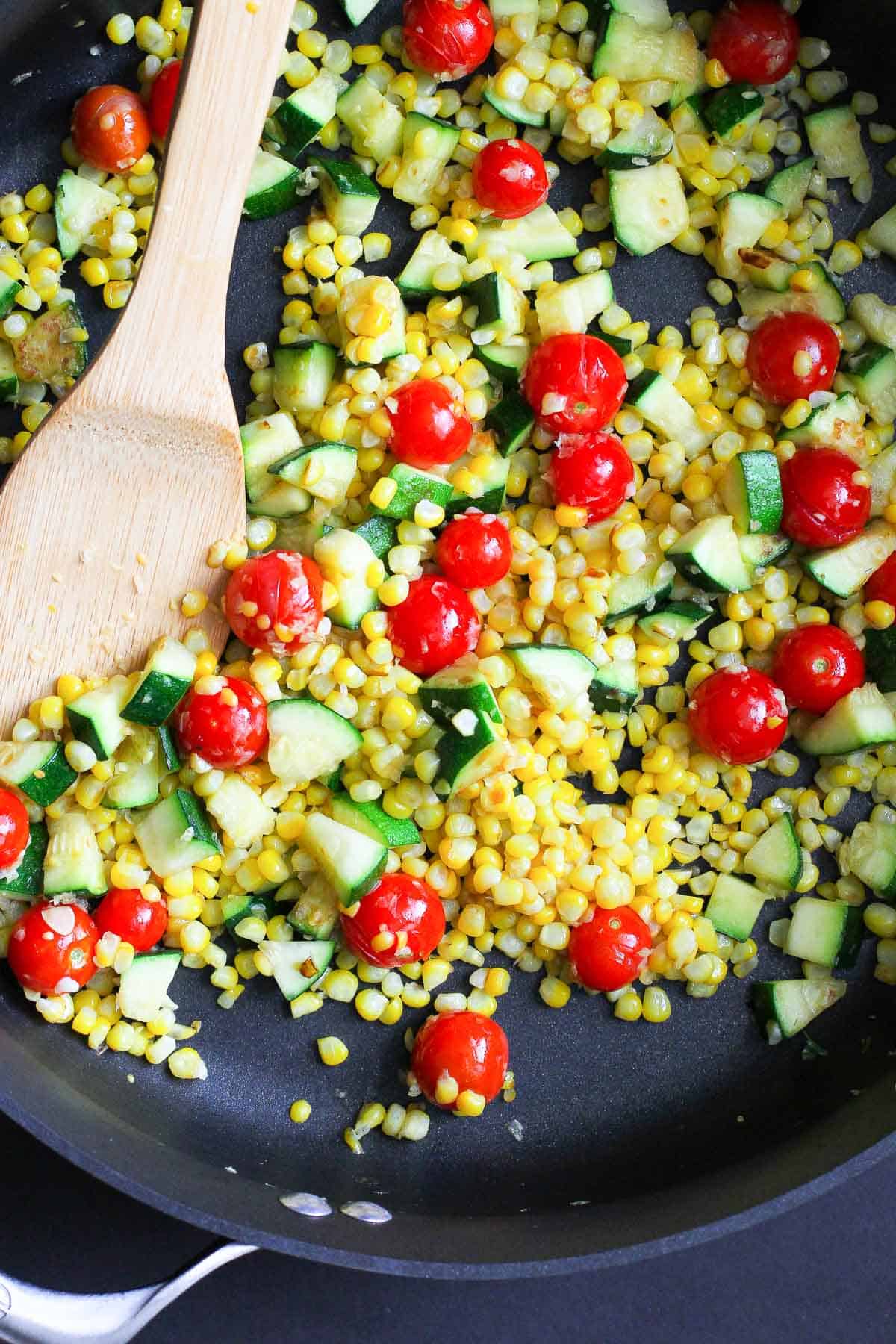Zucchini, corn kernels and cherry tomatoes in a skillet.