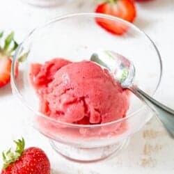 Glass bowl with a scoop of strawberry ice cream, surrounded by fresh strawberries.