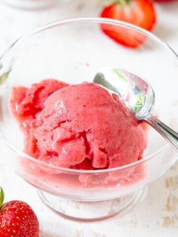 Glass bowl with a scoop of strawberry ice cream, surrounded by fresh strawberries.