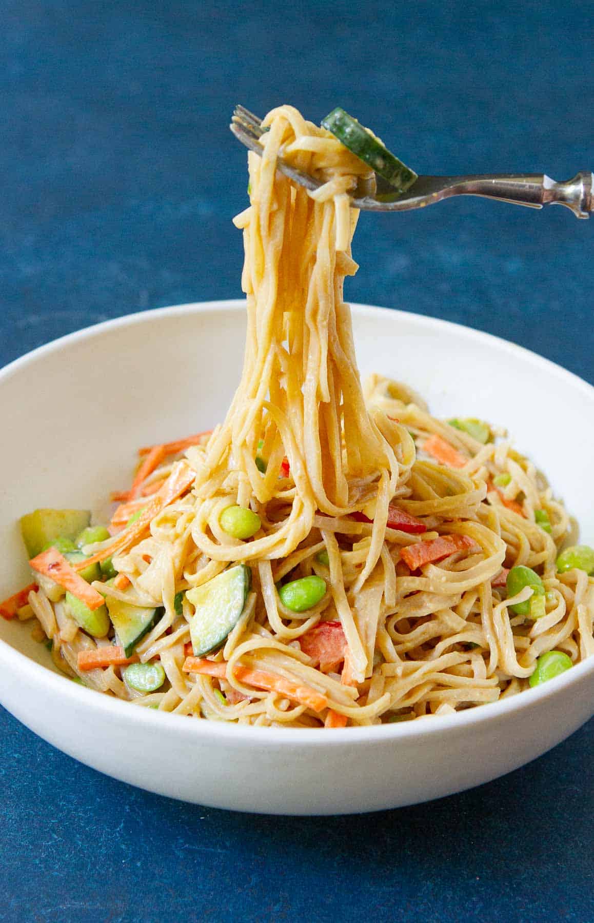 Peanut butter noodles with vegetables in a white bowl, with a fork.