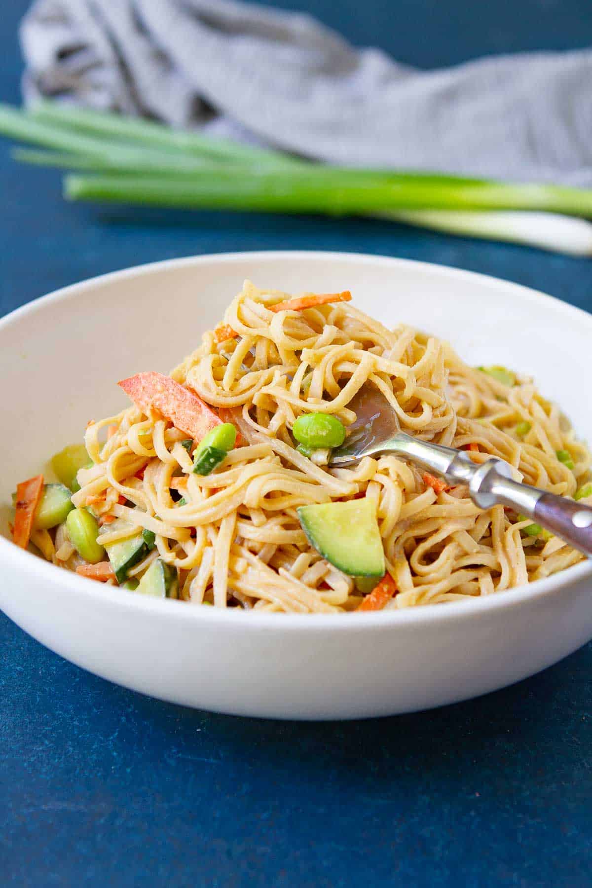 Vegan peanut noodles with vegetables in a white bowl.