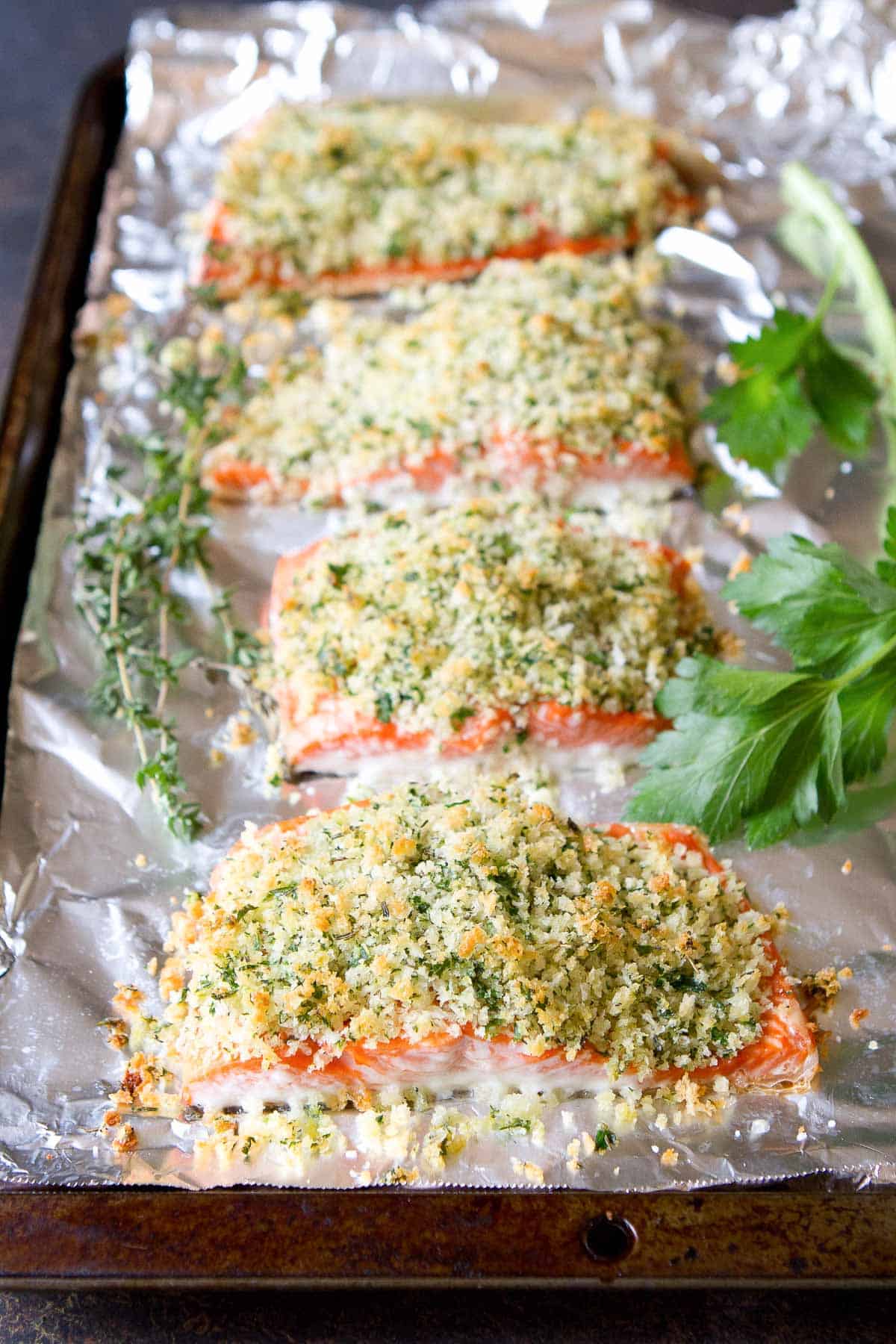 Salmon fillets on a foil-lined baking sheet, each topped with herb Parmesan crust
