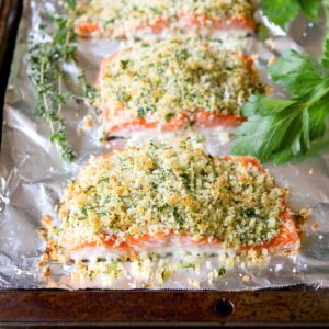 Salmon fillets on a foil-lined baking sheet, each topped with herb Parmesan crust