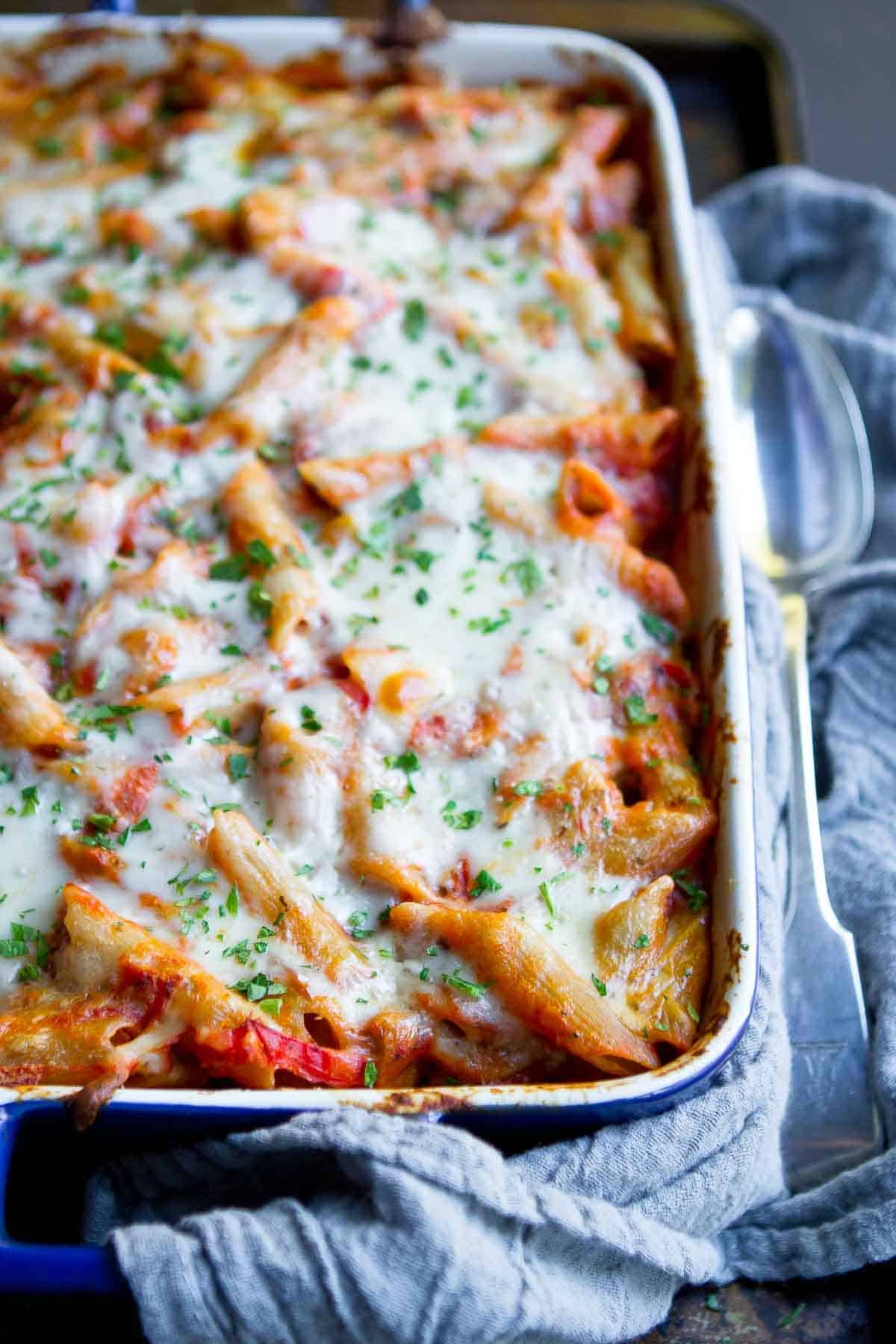 A blue casserole dish filled with baked pasta with sausage and cheese.