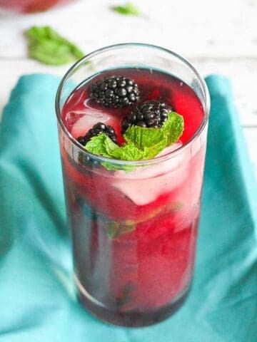 Blackberry tea and fresh blackberries in a tall glass, with a turquoise napkin.