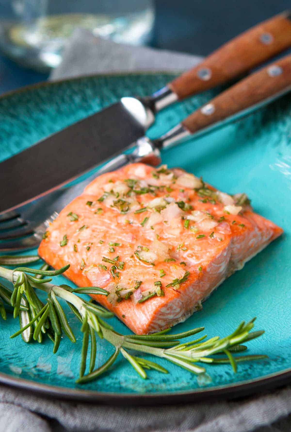 Glazed salmon fillet on a blue plate with a spring of rosemary.