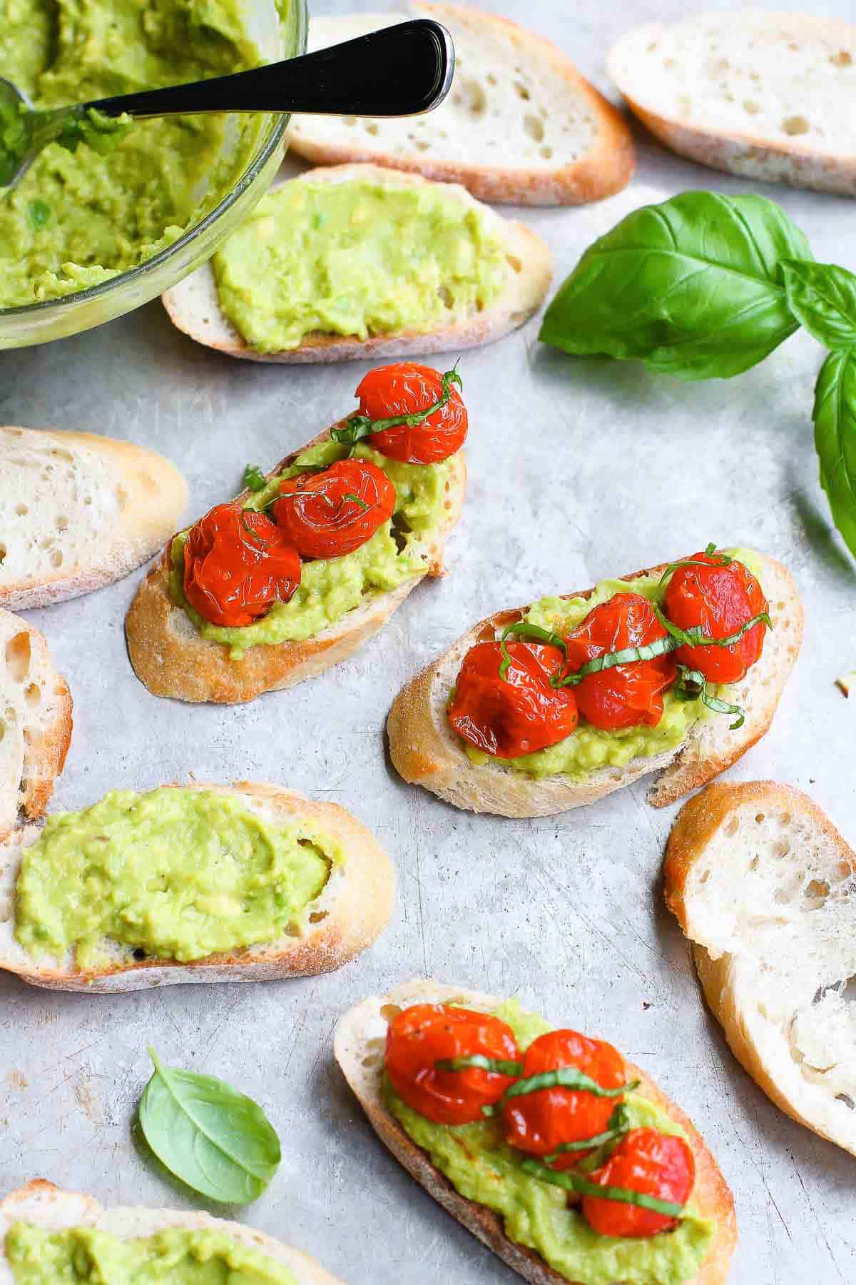 Toasted baguette slices, topped with mashed avocado and cooked tomatoes.