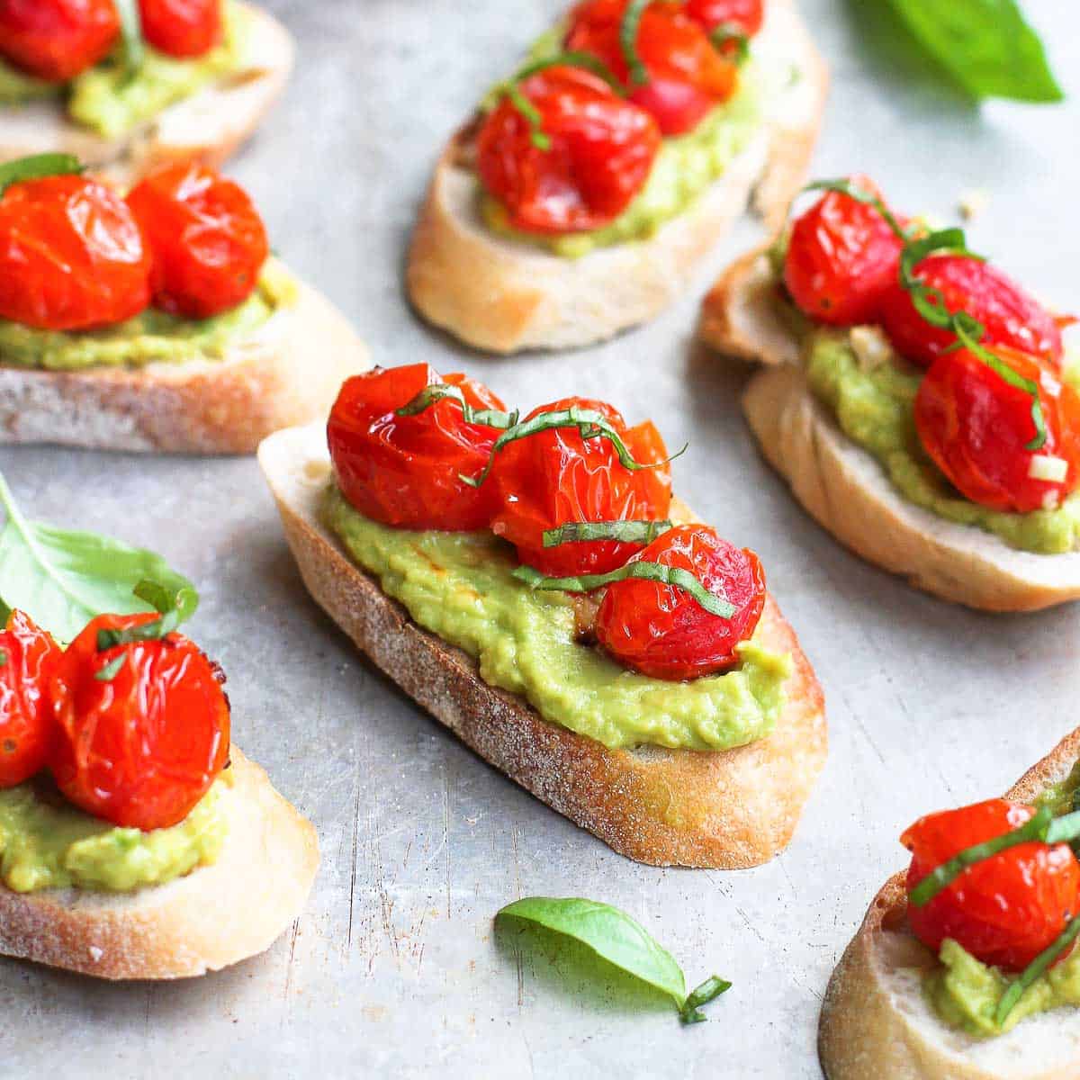 Baguette slices topped with smashed avocado and roasted tomatoes.